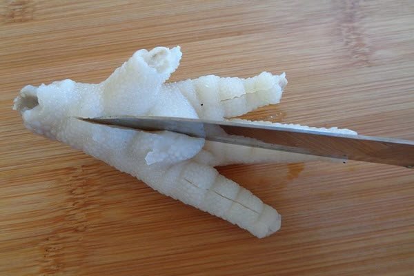 Để rút xương chân gà, bạn đặt chân gà lên thớt, dùng dao khía lên từng ngón chân gà Để rút xương chân gà, bạn đặt chân gà lên thớt, dùng dao khía lên từng ngón chân gà